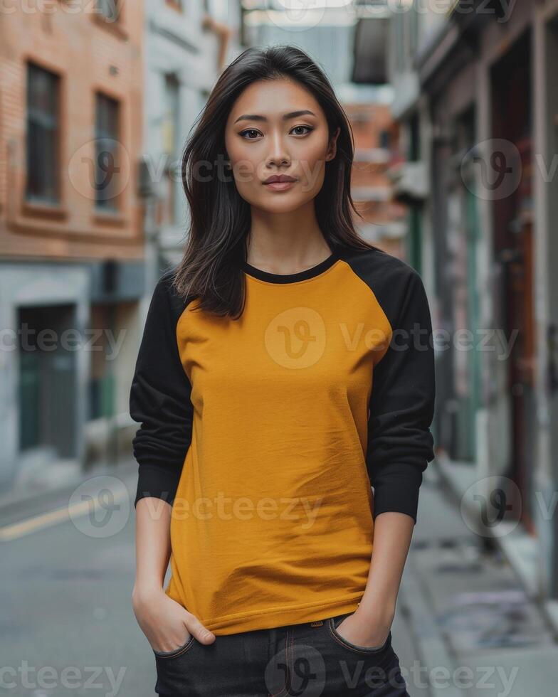 A woman wearing a mustard yellow raglan shirt with black sleeves poses in a city alleyway photo