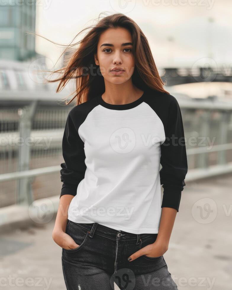 A young woman in a white raglan shirt with black sleeves poses on a city street photo
