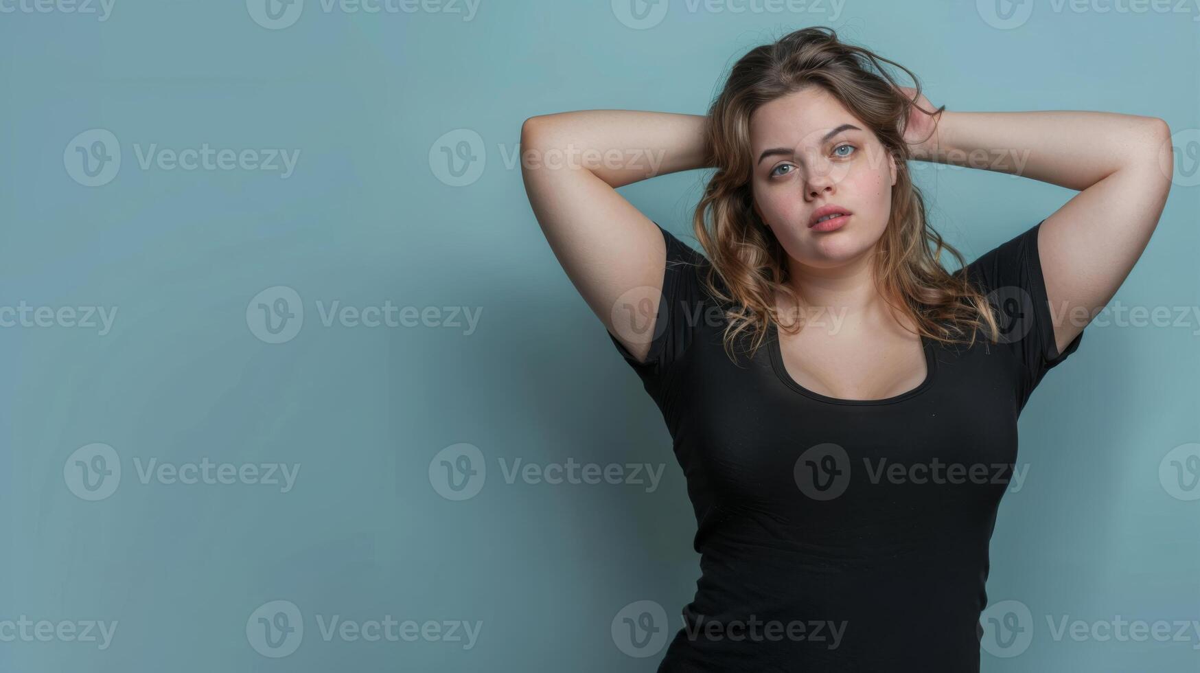 A woman with long, wavy hair wears a black t-shirt against a muted blue backdrop photo