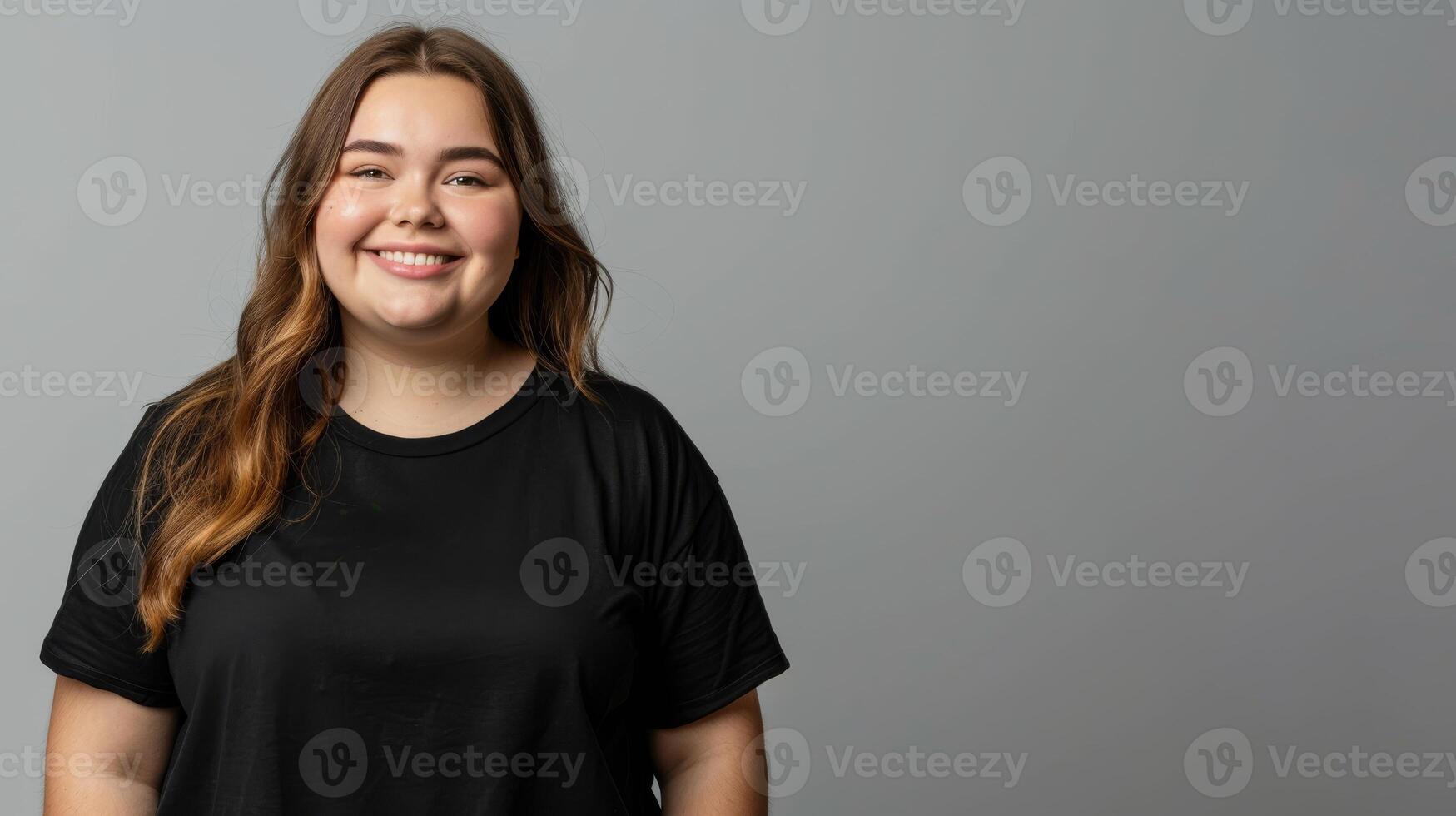 A smiling woman in a black t-shirt stands against a grey backdrop photo