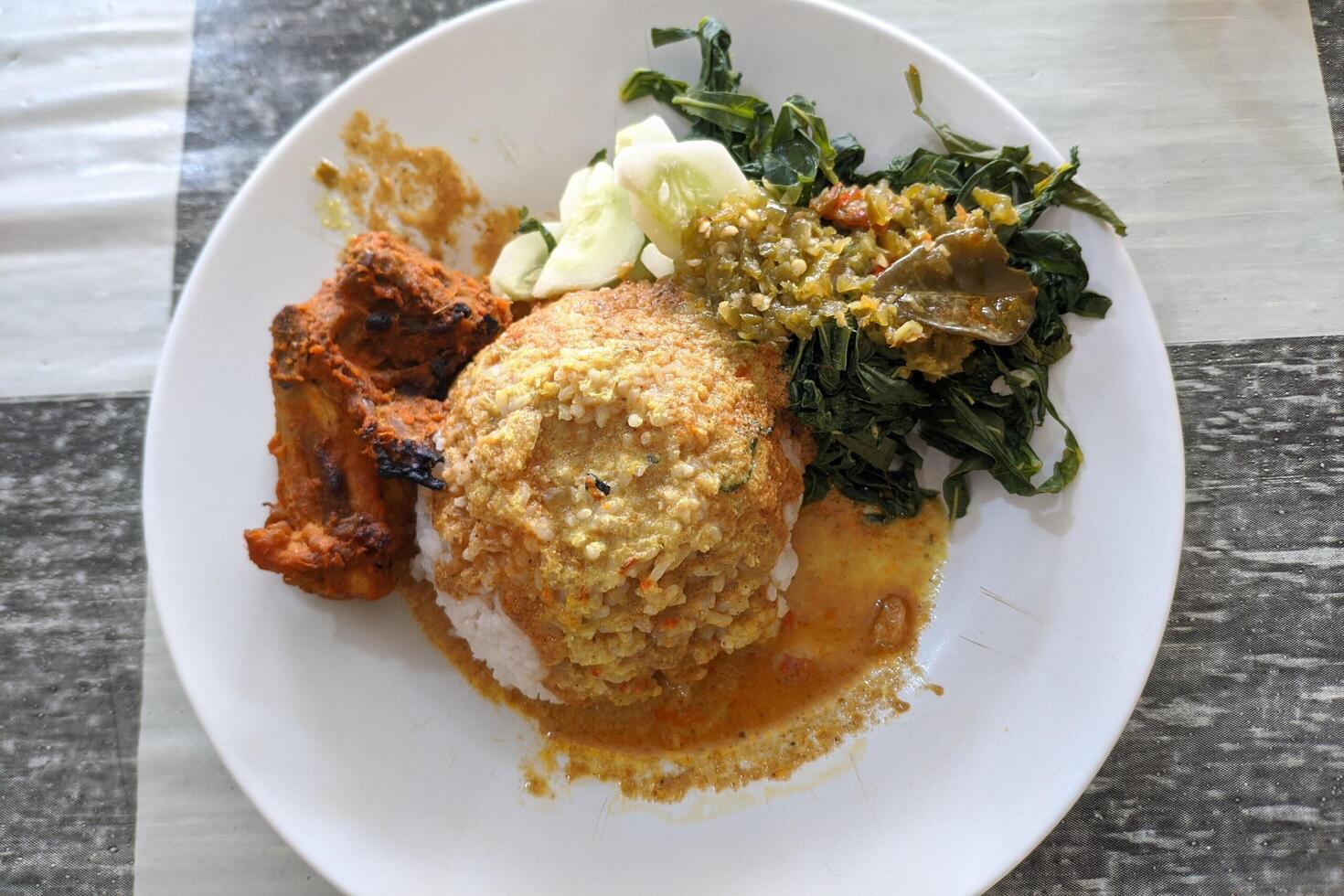 a portion of nasi Padang served on a table. which consists of grilled chicken, cucumber, cassava leaves and rice covered in a very delicious sauce. typical food from Sumatra, Indonesia photo