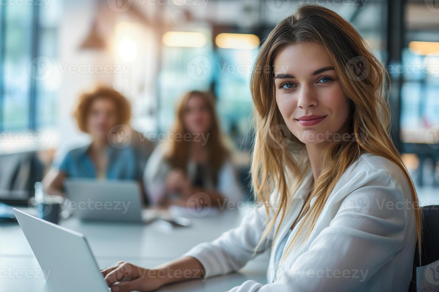 Beautiful young business woman working on laptop in the office with colleagues in the background photo