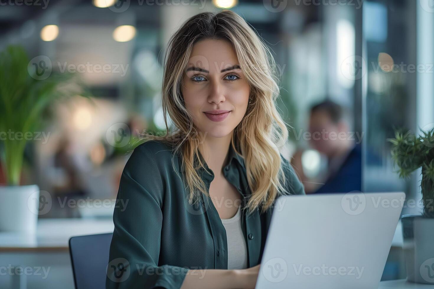 Beautiful young business woman working on laptop in the office with colleagues in the background photo