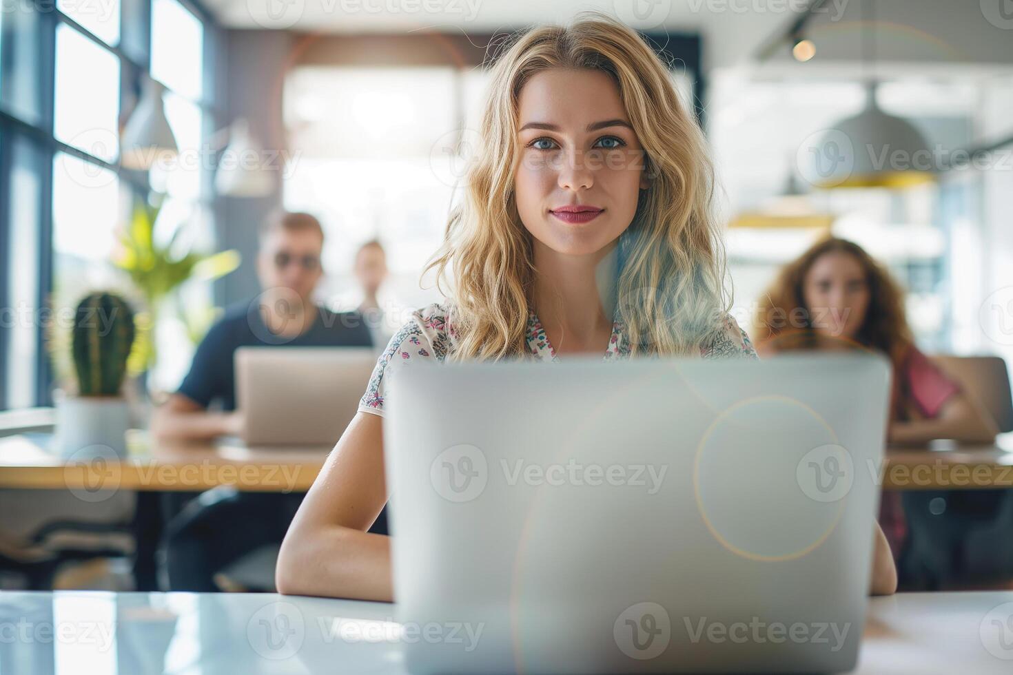 Beautiful young business woman working on laptop in the office with colleagues in the background photo
