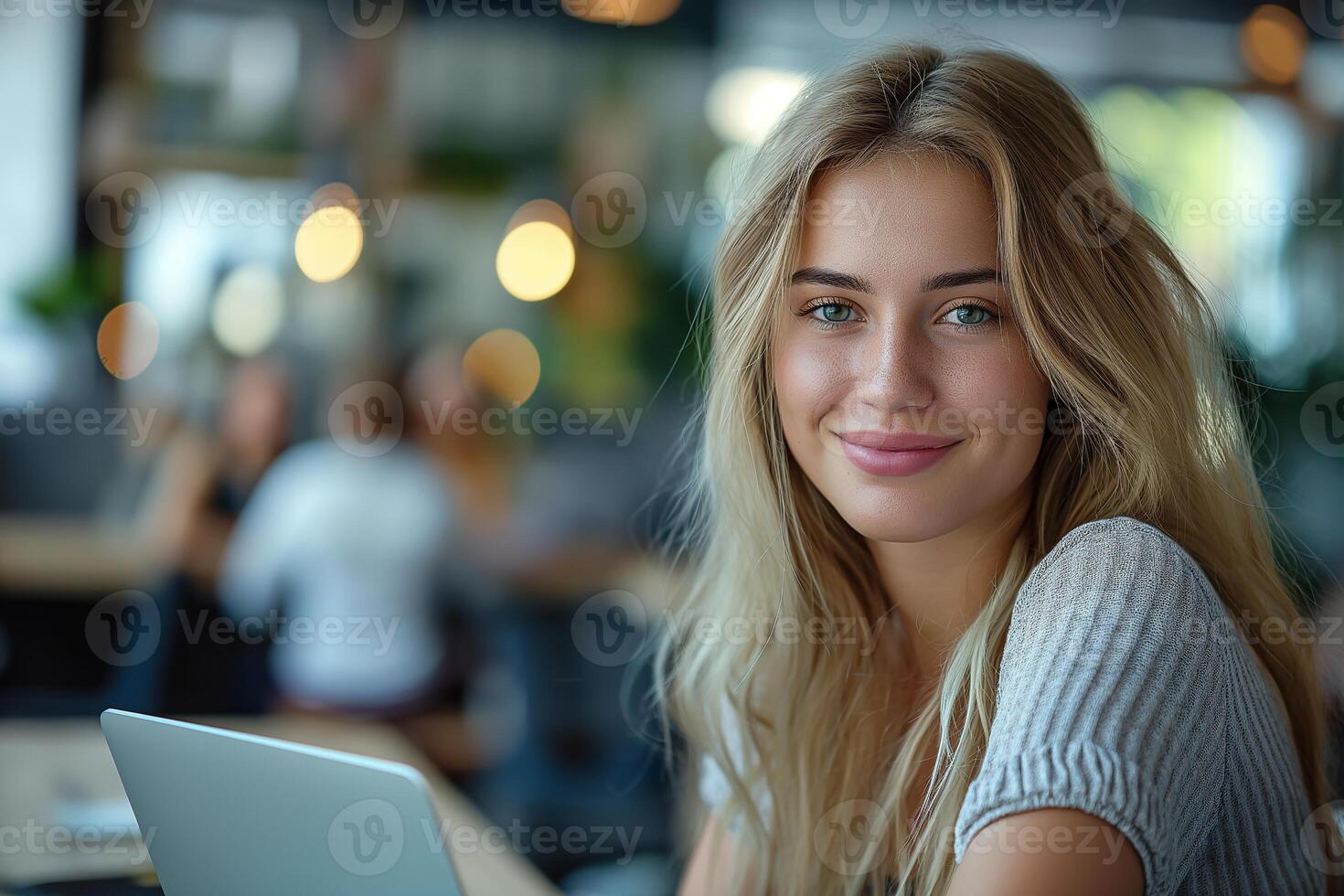 A young woman in a blue blouse is smiling while working on a laptop at an office desk photo