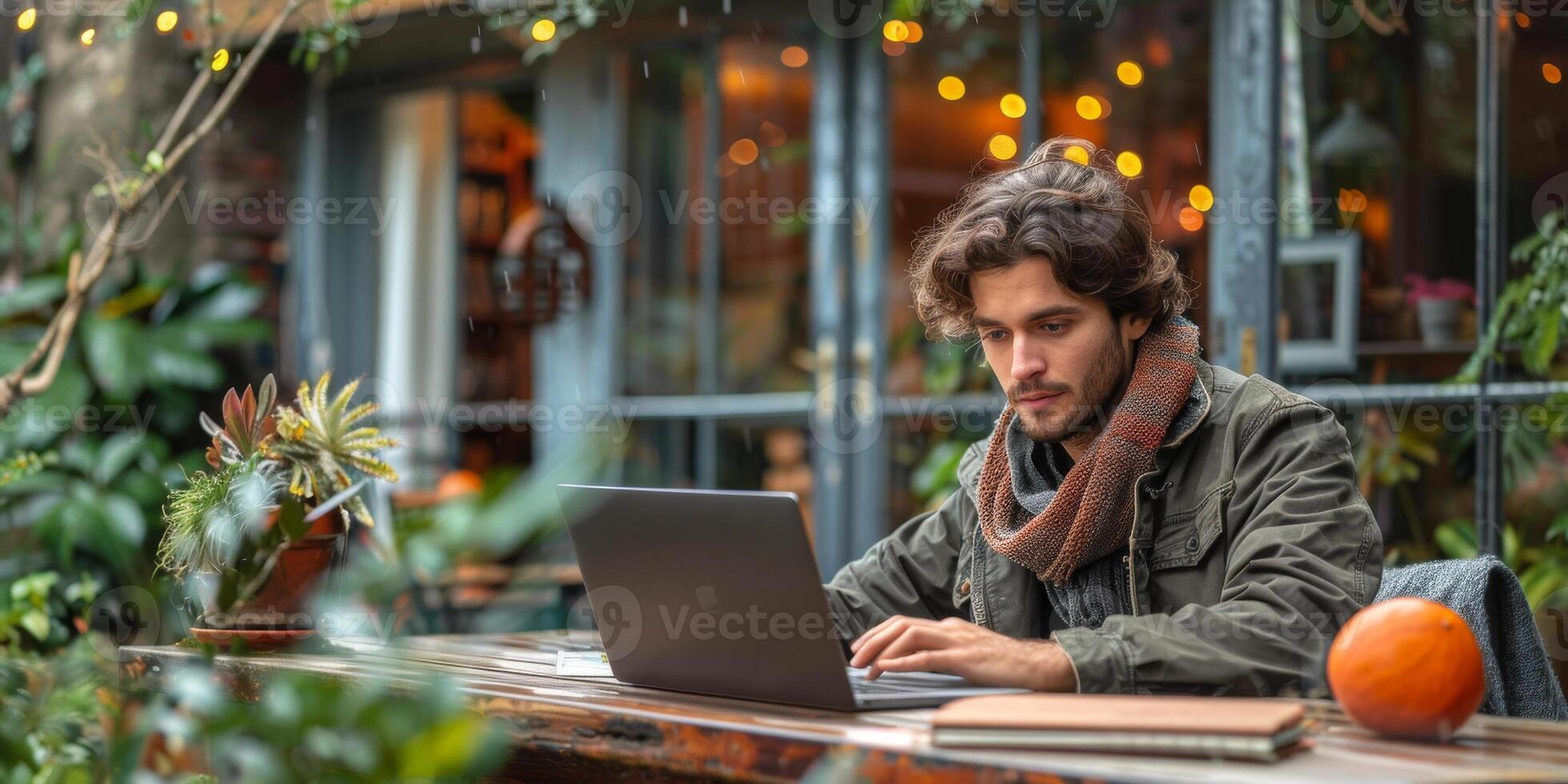 A man with a beard is sitting at a table, using a laptop computer indoors photo