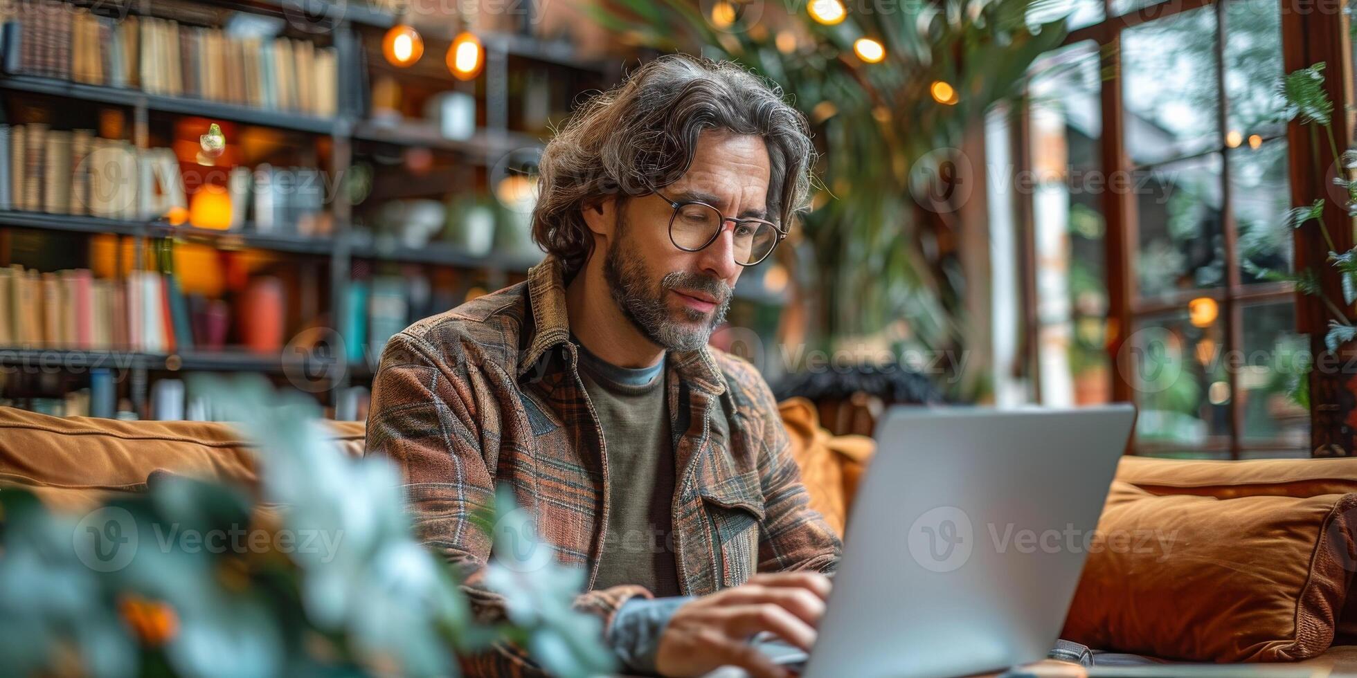 The man with a beard is sitting on a couch, using a laptop photo