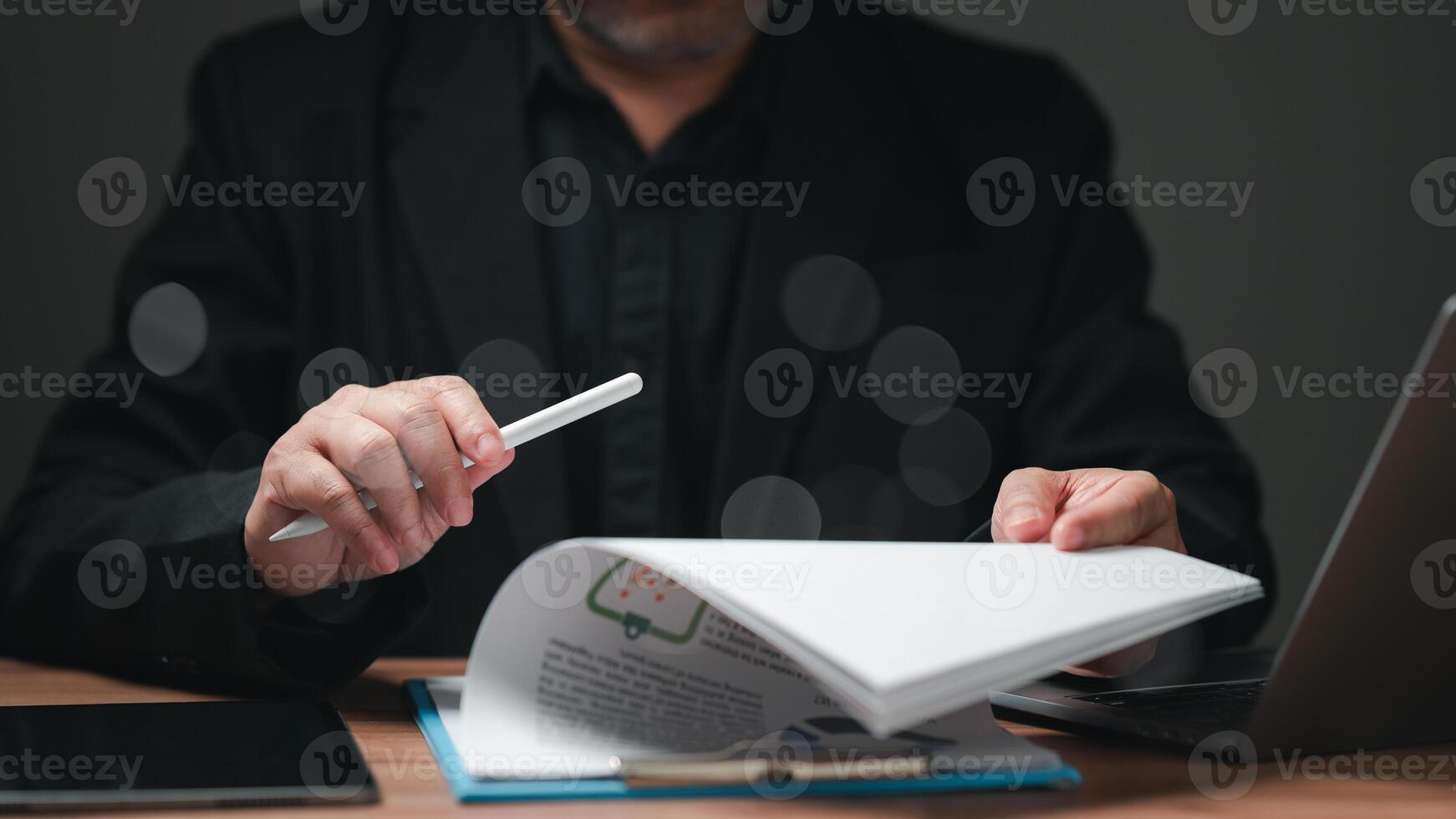 A businessman is sitting at a desk with a laptop and a piece of paper. He is holding a pen and he is writing something, financial, paperwork photo