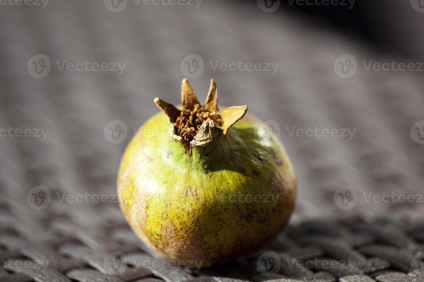 An unripe green pomegranate on a wicker brown table in the sunlight. An autumn fruit. Healthy food. Horizontal photo