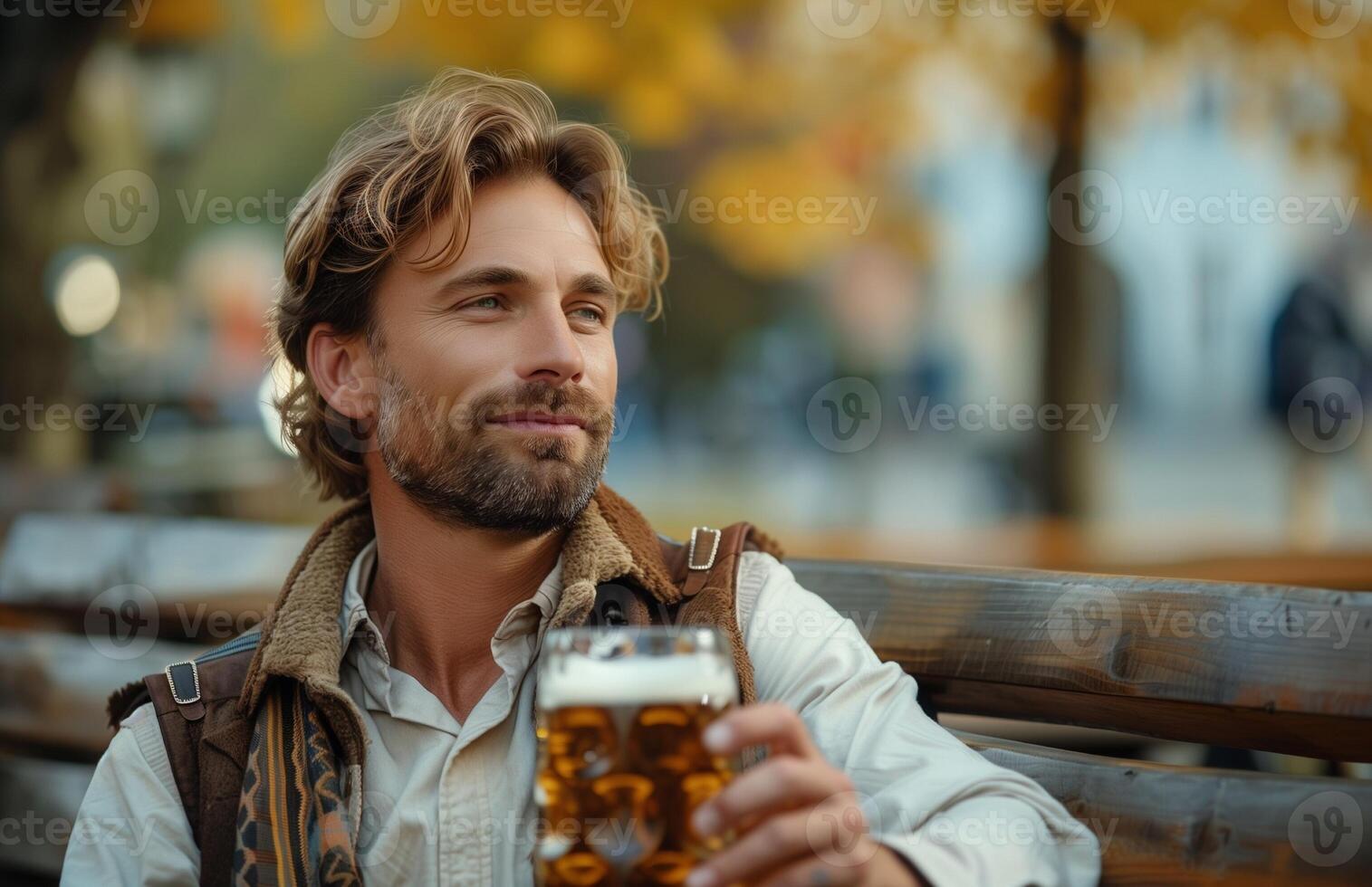 Handsome man in traditional Bavarian attire drinking beer from a large glass while sitting on a bench photo