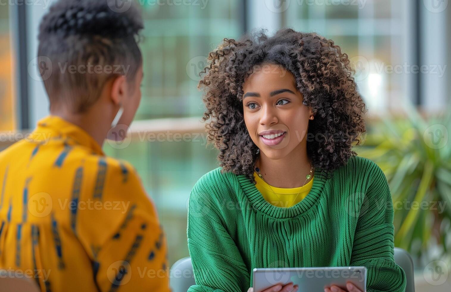 A curly haired young woman in a green sweater interviews in an office with a tablet photo