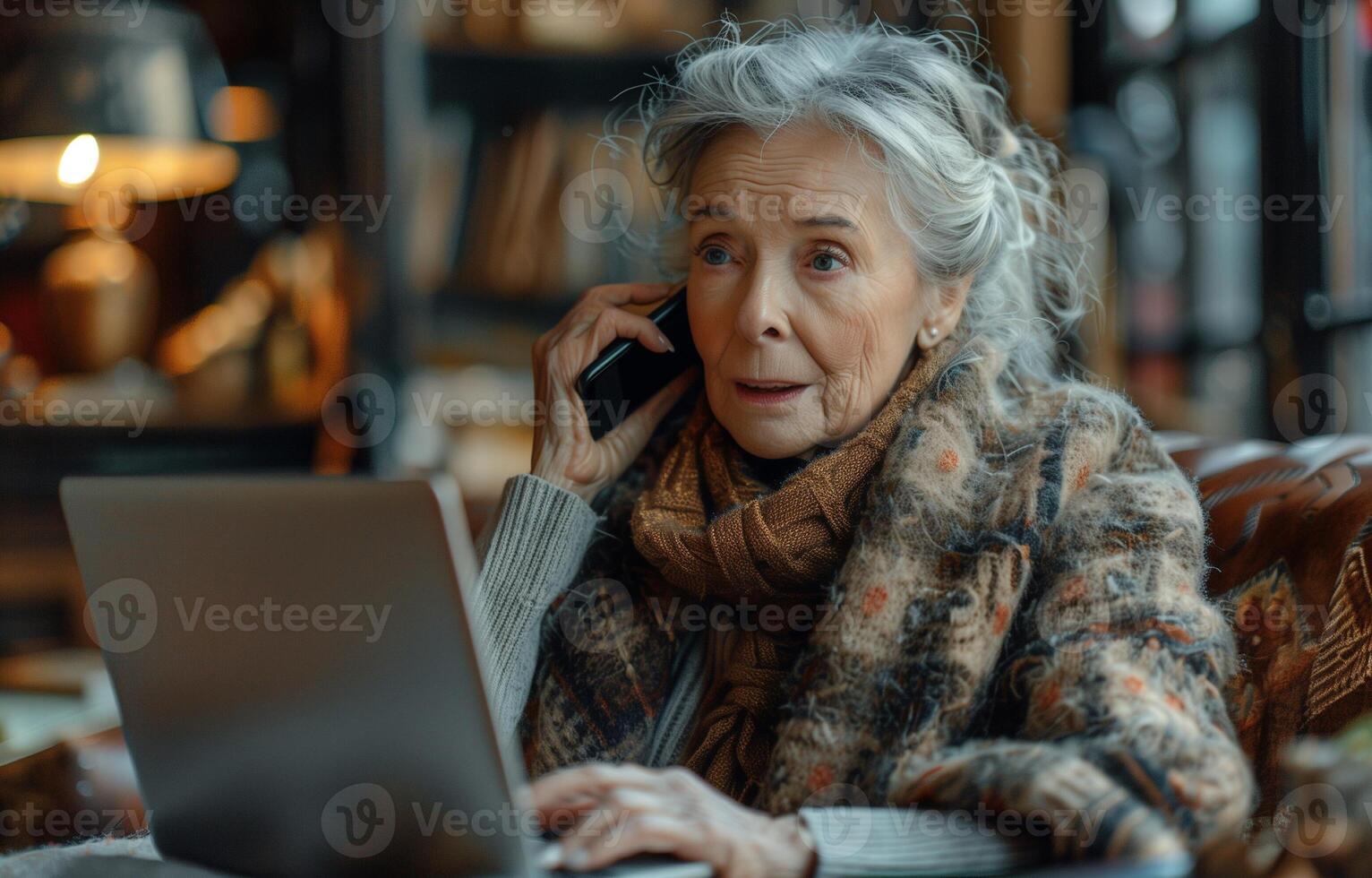 Elderly woman multitasking with a laptop and mobile phone, engaging in communication from home photo