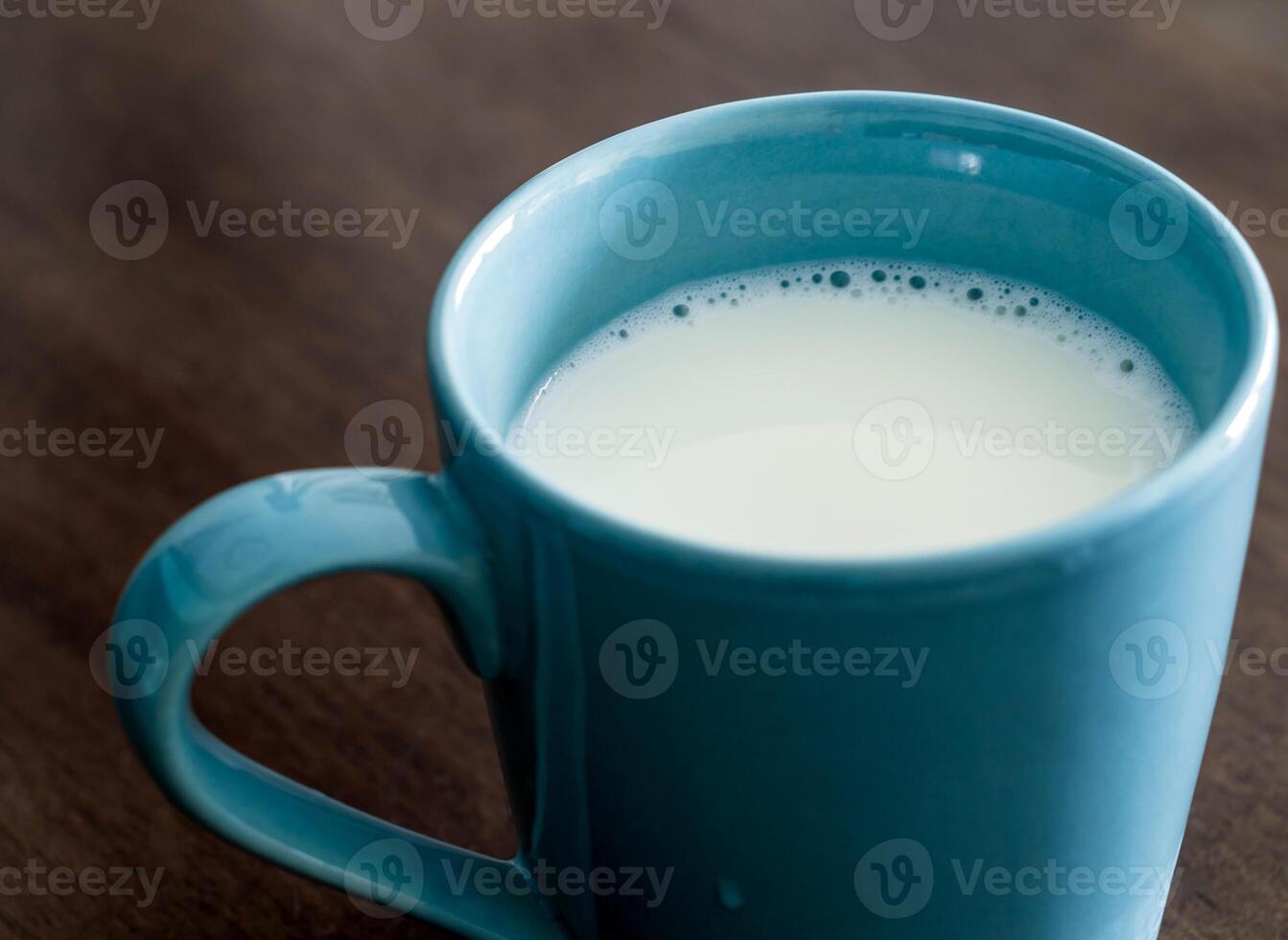 Milk in a blue cup on the wooden and top glass table photo