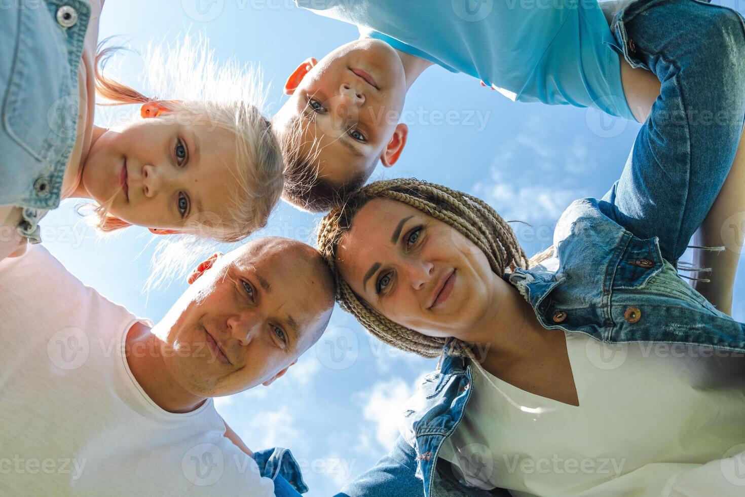 A family huddles closely view from below, their faces framed by the blue sky, capturing a moment of joy and togetherness and used for national siblings day, family time, bonding. photo