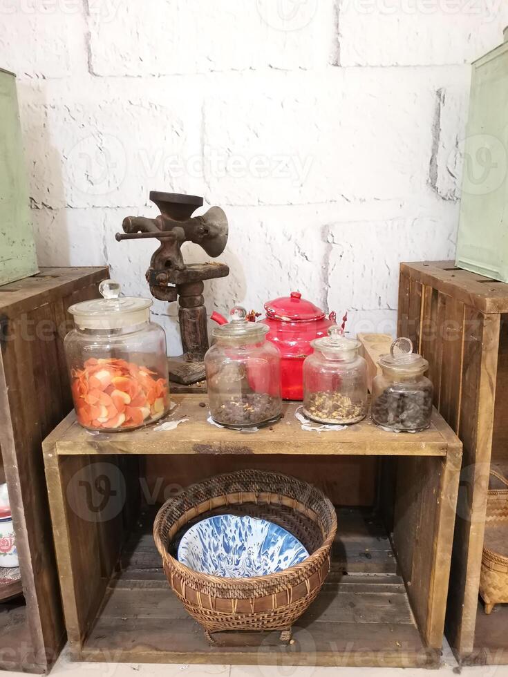 Antique coffee grinders and old teapots are arranged next to traditional food jars on wooden boxes. Traditional Indonesian kitchen utensils and food basket. Old thing. photo
