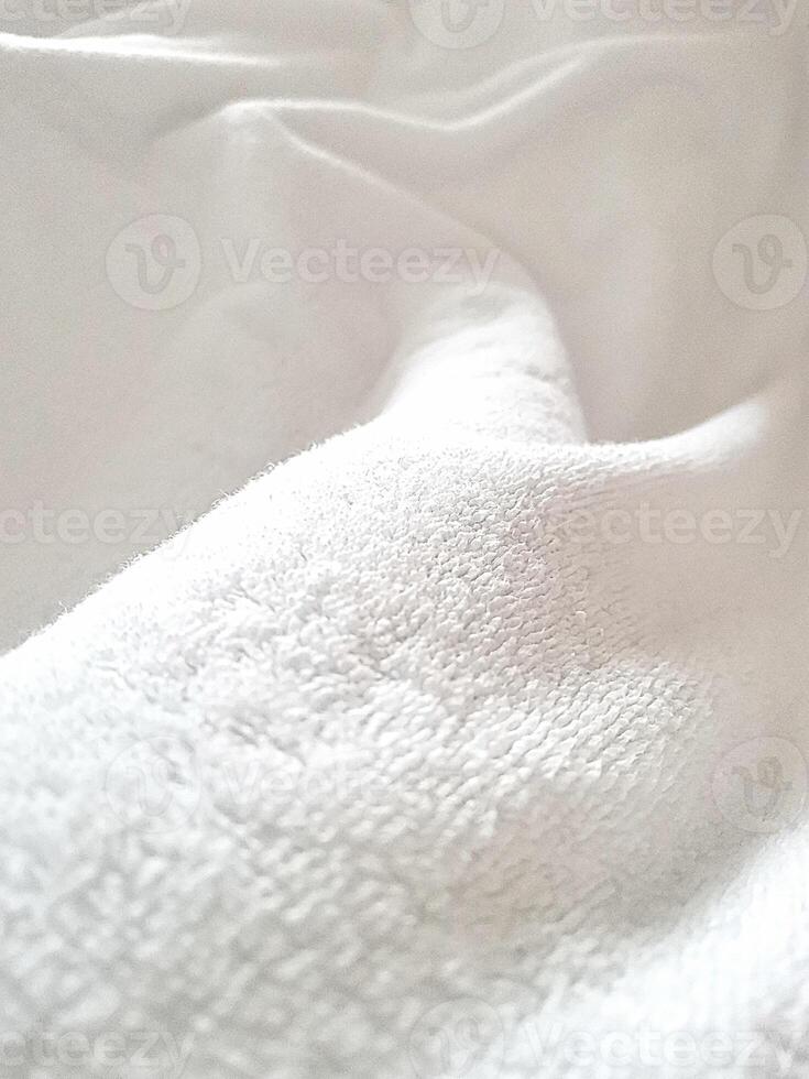White delicate soft background of plush fabric. Texture of white soft fleecy blanket textile with twisted folds. photo