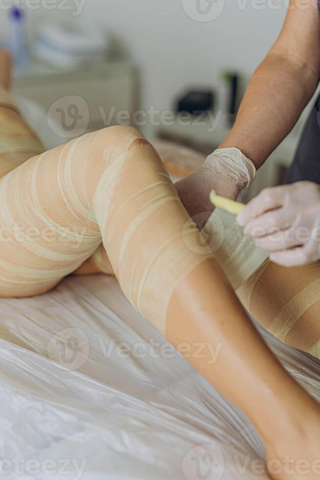 Professional cosmetologist woman removes all bandages after the procedure of wrapping in a beauty salon. photo