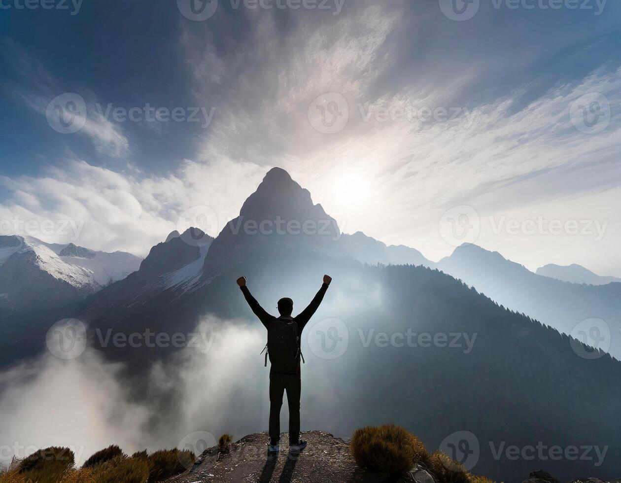 Silhouette of a man standing with his arms raised on a smoky mountain peak in the background. photo