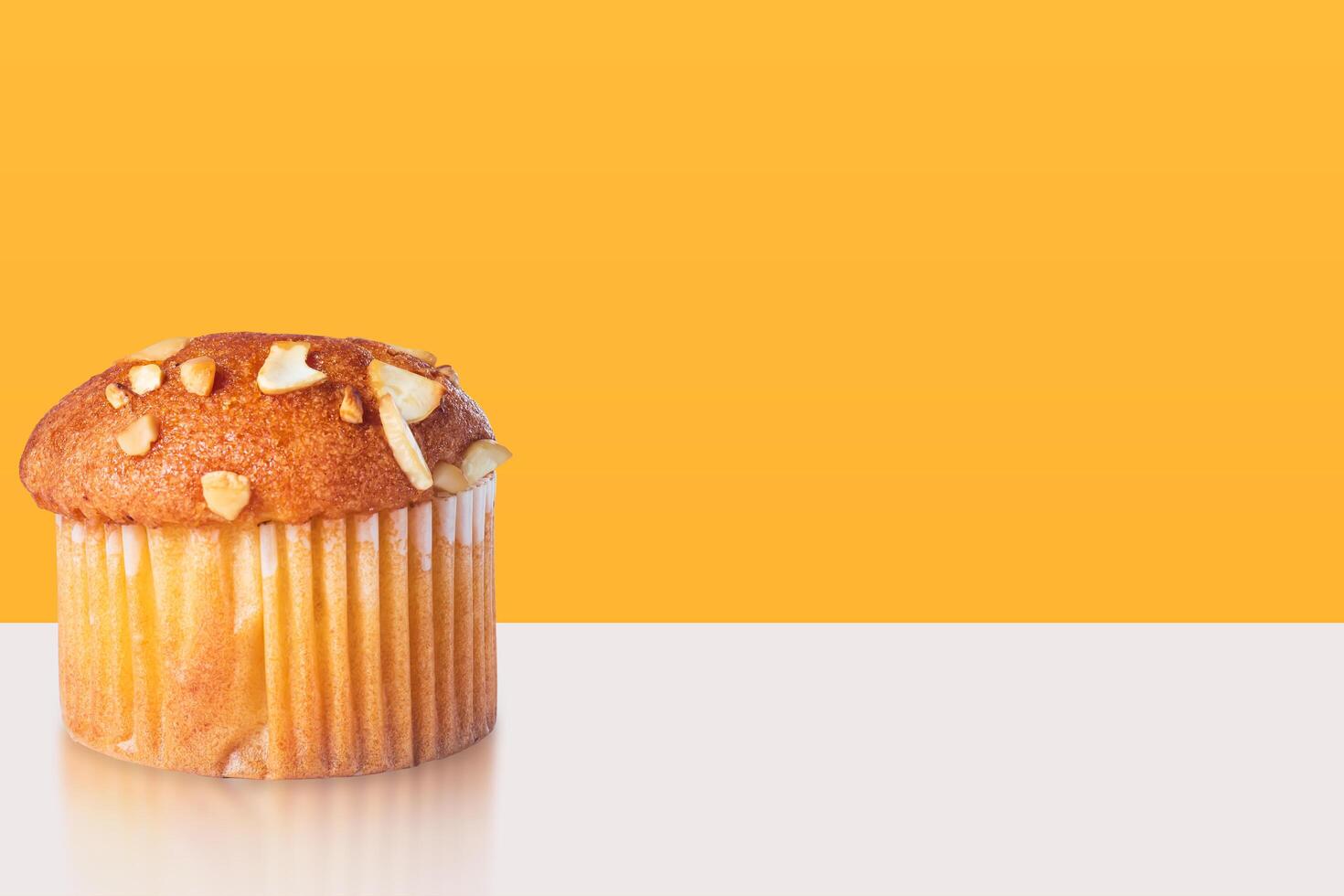 Delicious almond topped cupcake muffin with reflection on white table with yellow background. Template for product presentation. photo