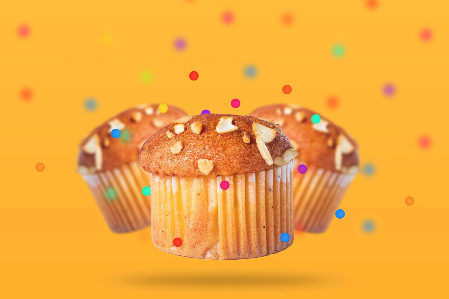 Three delicious almond topped muffins with colorful confetti float on a vibrant yellow background. Closeup photo