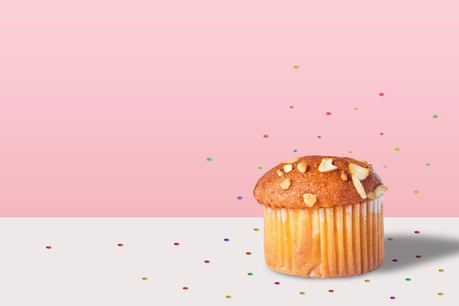 Almond muffin with confetti isolated white table on pink background. Closeup photo