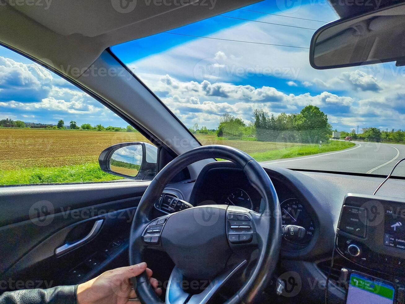 Man hands holding car steering wheel while driving through countryside landscape photo