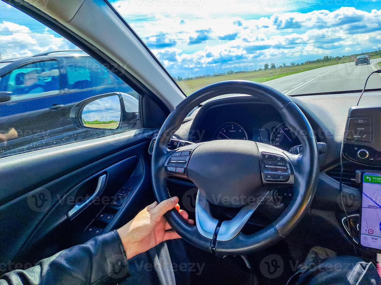Man hands holding car steering wheel while driving through countryside landscape photo