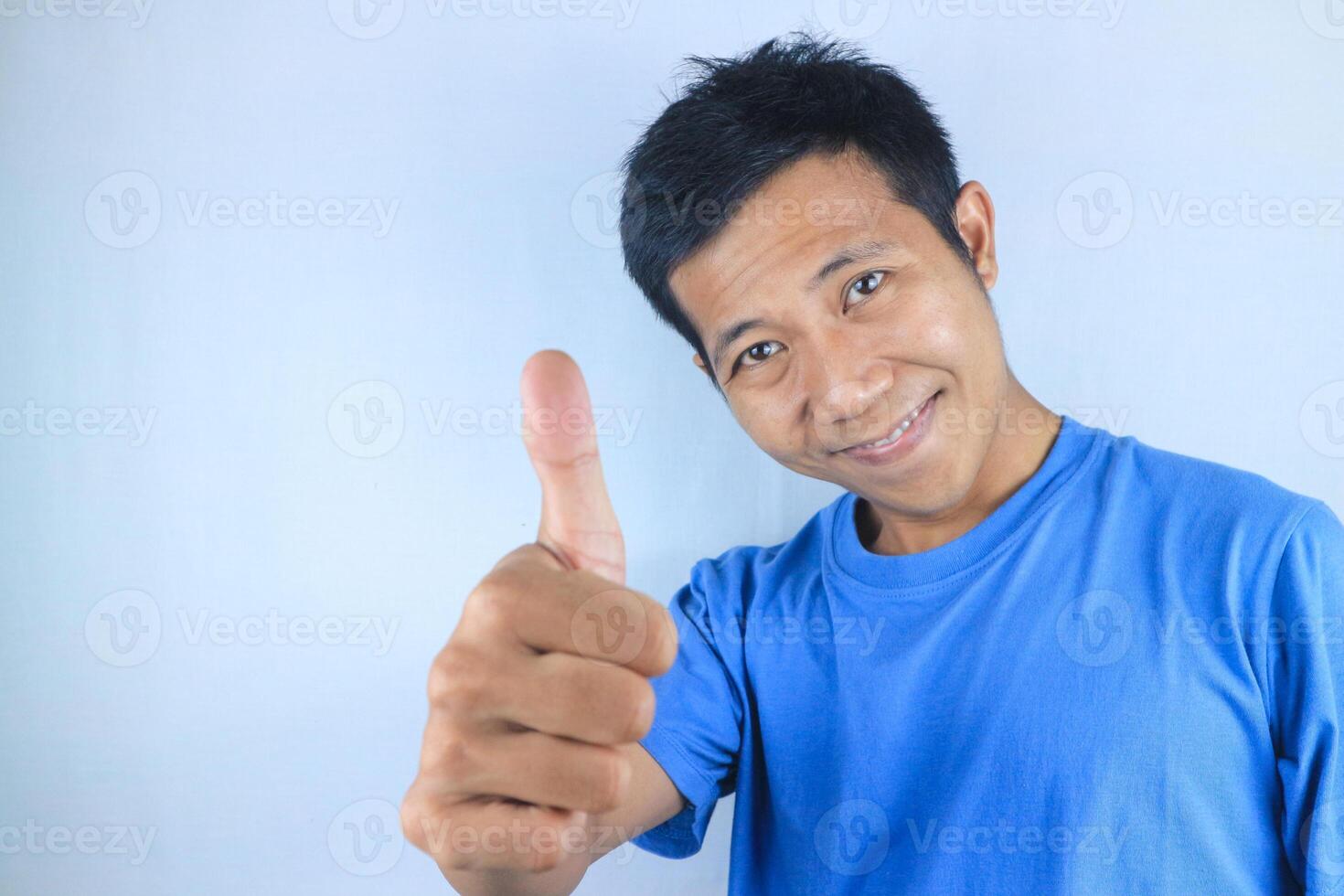 Funny face expression young asian man looking at camera while giving thumps up gesture photo