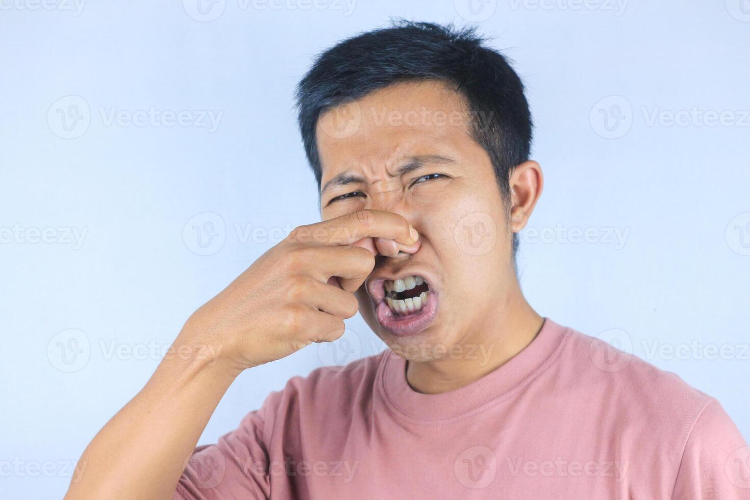 funny expression of young asian man covering his nose because of disgusting smell photo