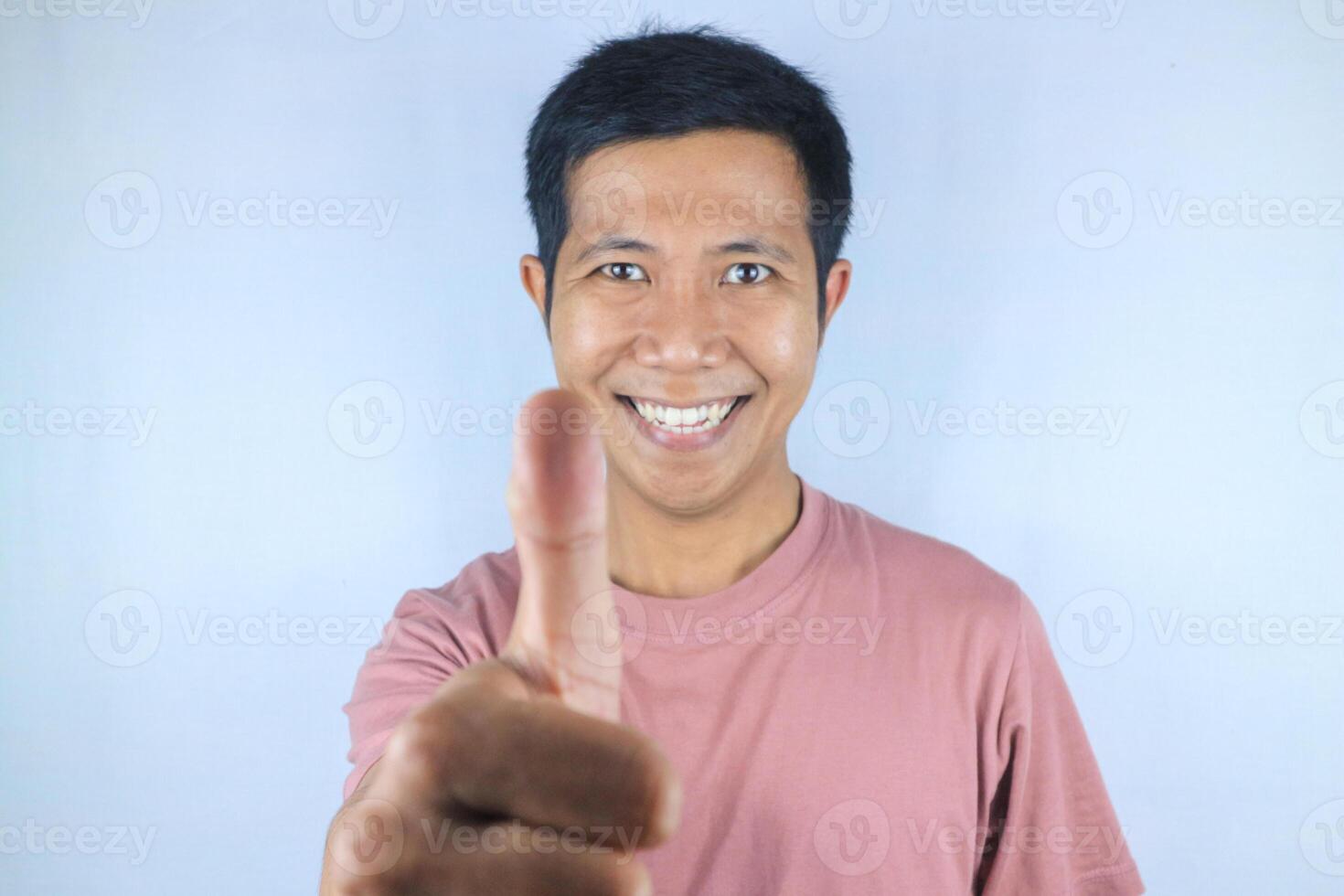 Funny face expression young asian man looking at camera while giving thumps up gesture photo