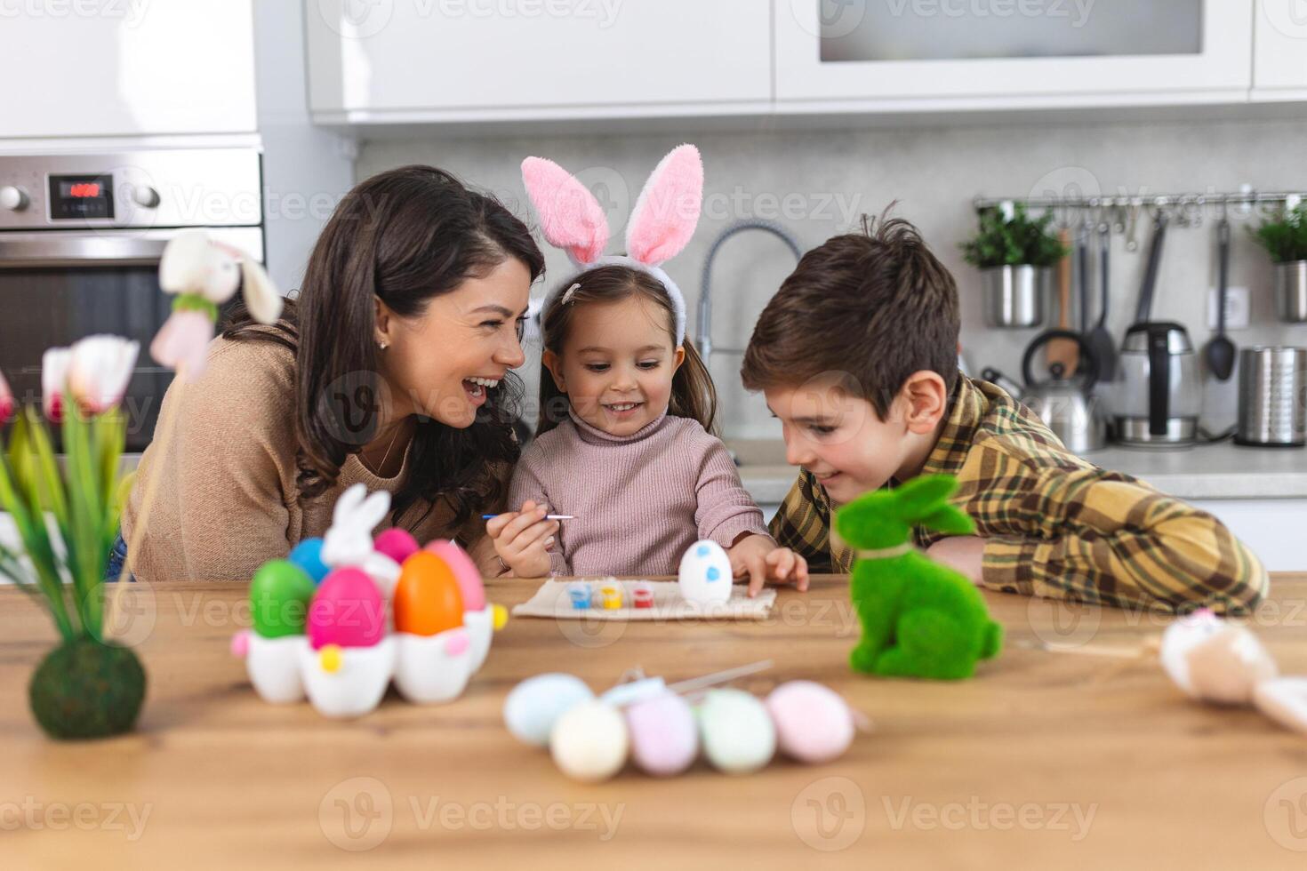 Mother, son and daughters are painting eggs. Happy family are preparing for Easter. Cute little child girl wearing bunny ears. photo