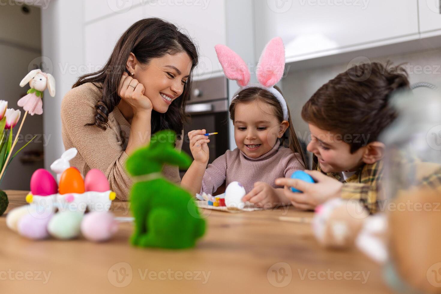Easter Family traditions. Loving young mother teaching happy little kids to dye and decorate eggs with paints for Easter holidays while sitting together at kitchen table photo