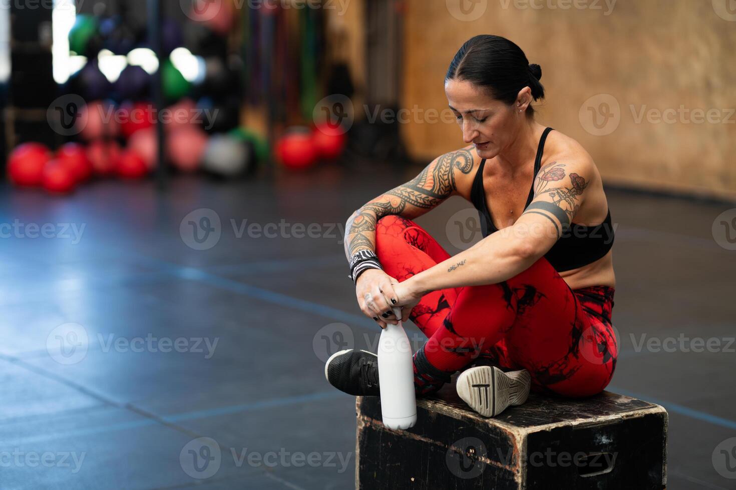Tired woman looking down sitting on a box in gym photo