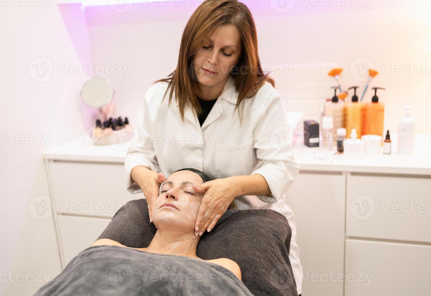 Female beautician massaging face of woman in beauty salon photo