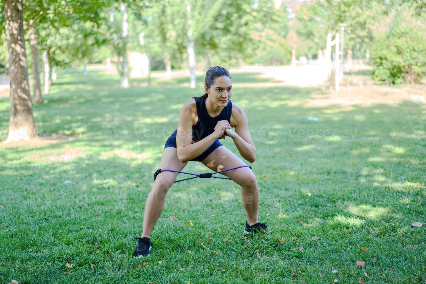 A woman is doing squat exercises with a resistance band in a park, focusing on fitness and strength photo