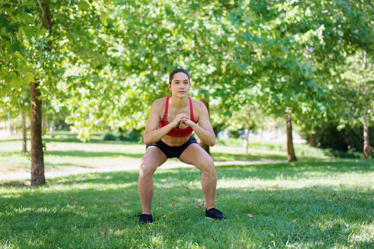 In the park, a woman is dedicated to a healthy lifestyle, displaying her commitment through squat exercises photo