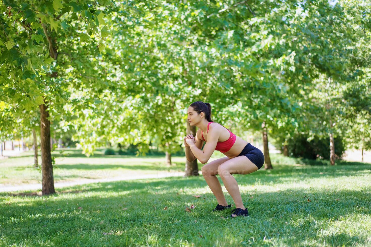 A woman is doing squats in a green park, showing an active and determined approach to fitness and health photo