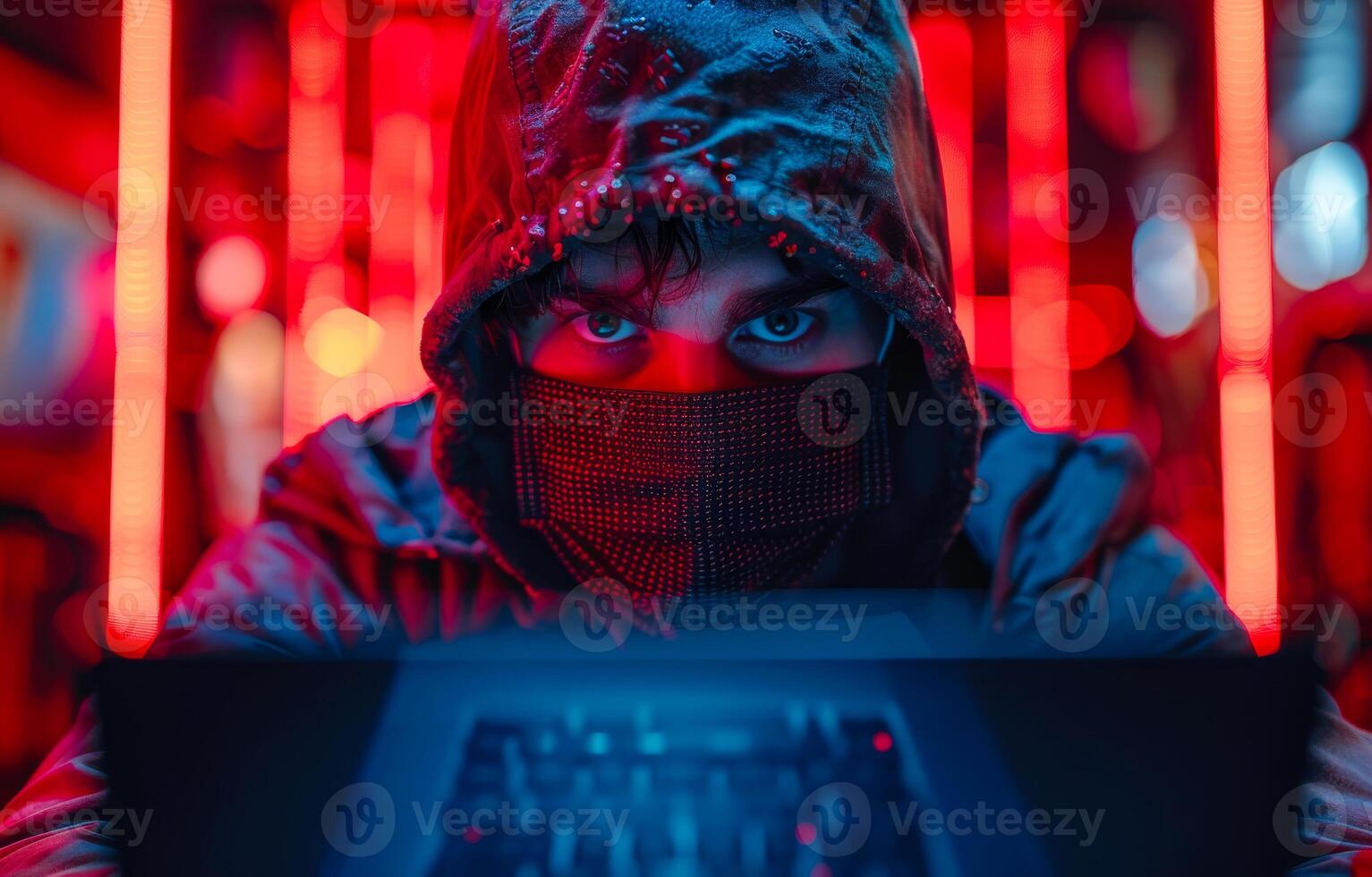 A man wearing a hoodie and a mask is looking at a computer screen photo