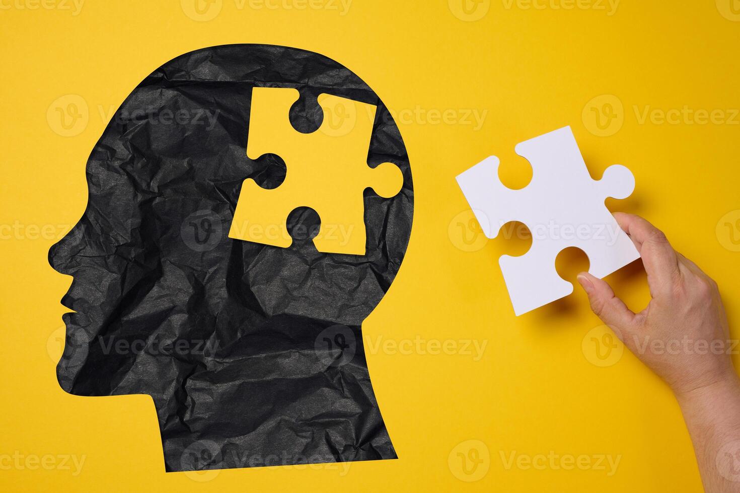 Silhouette of a human head holding a puzzle piece on a yellow background, representing mental health photo
