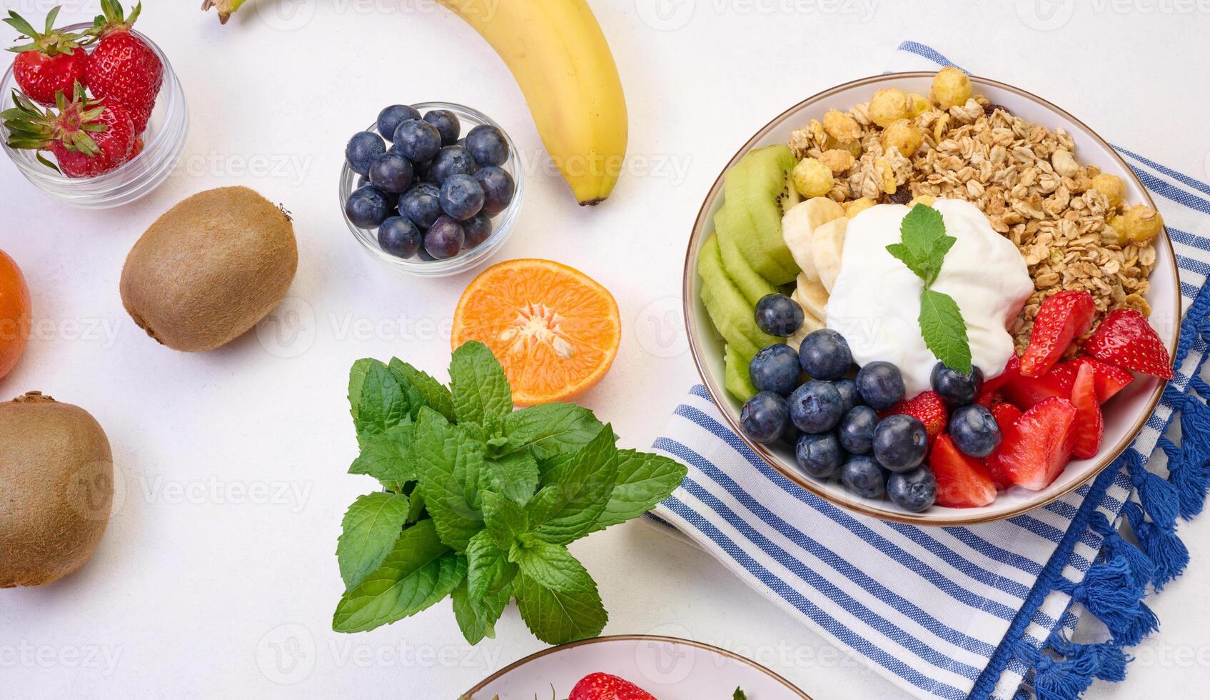 Granola with strawberries, kiwi, banana and blueberries in a round plate on a white table. photo