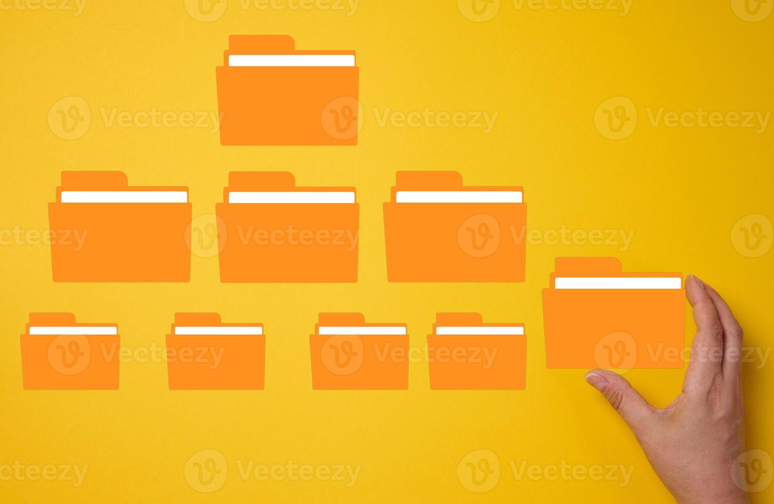 Hand holds a yellow folder over a yellow background with several folders. photo