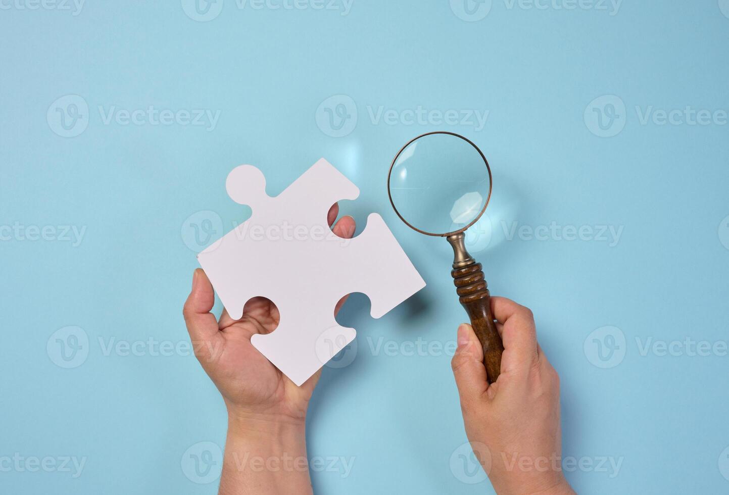 White empty puzzle and a magnifying glass in hand on a blue background photo