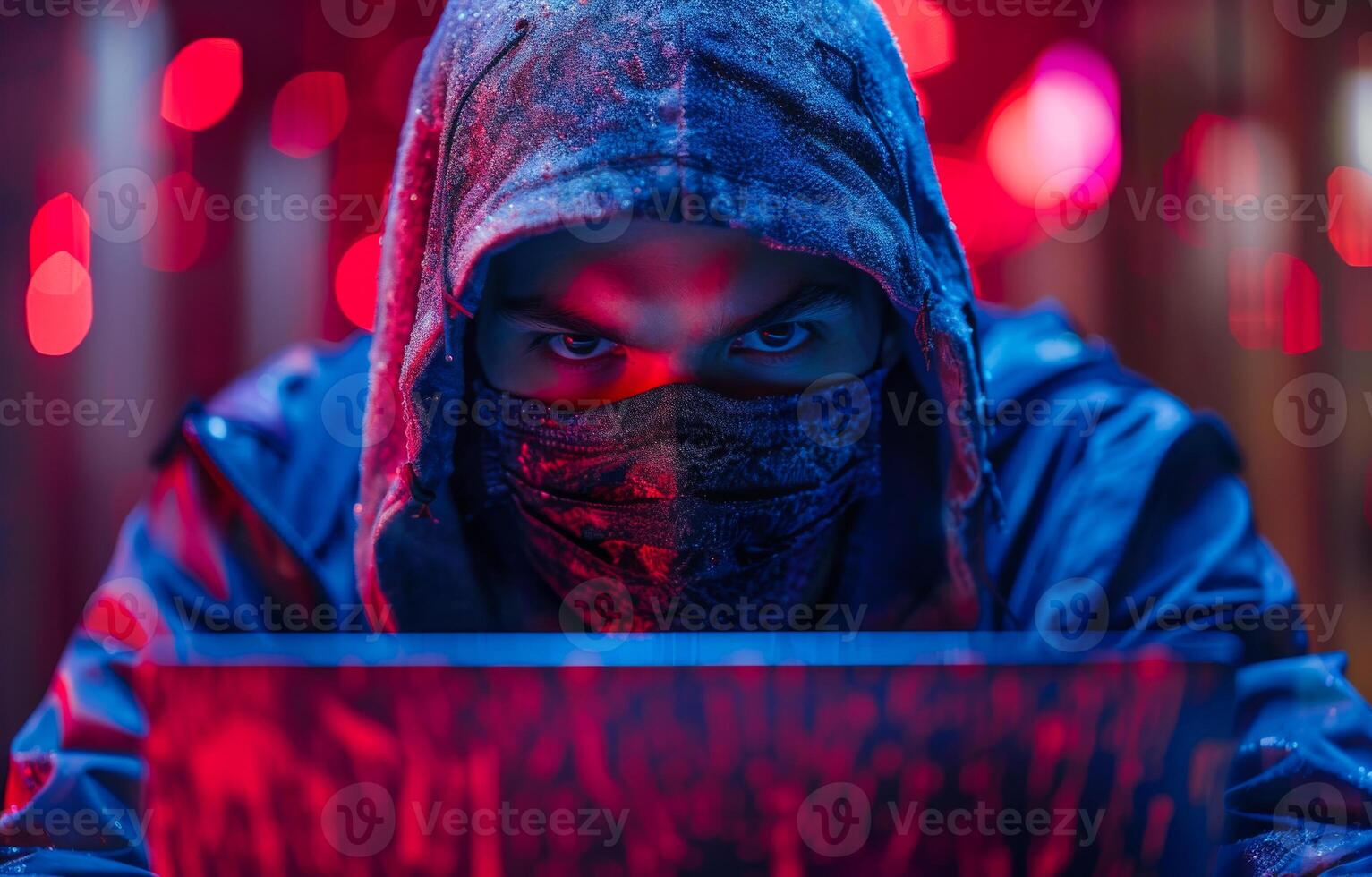 Masked Hacker Working On Laptop At Night. A hooded figure wearing a face mask and looking intently at a laptop screen. photo