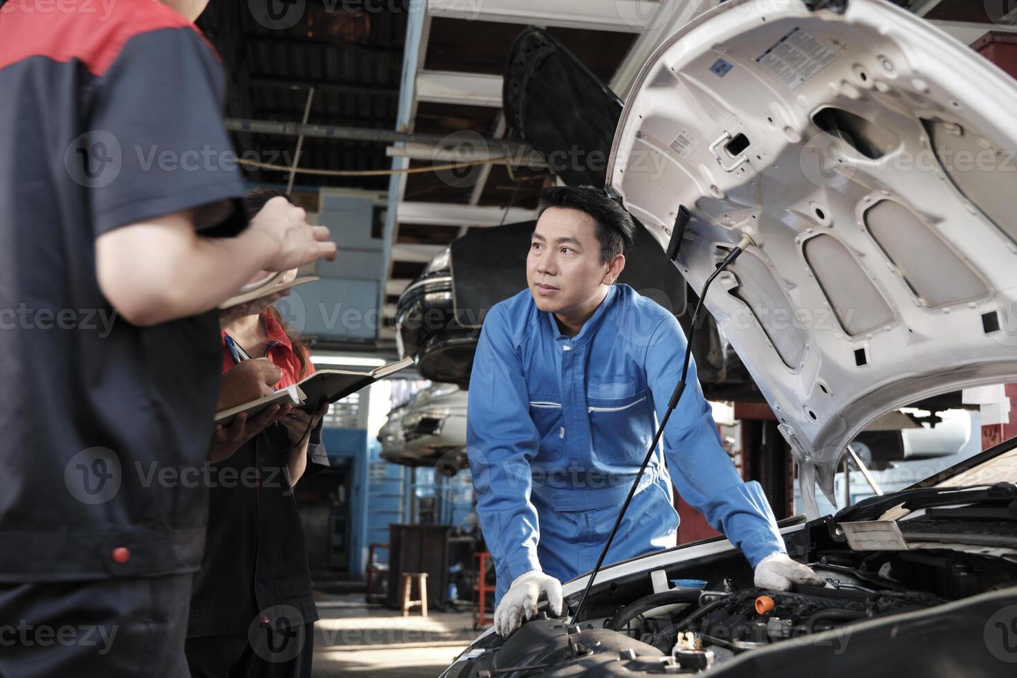 Asian male professional automotive engineer supervisor describes car engine maintenance and repair work with mechanic worker staffs team in fix service garage, specialist occupations in auto industry. photo