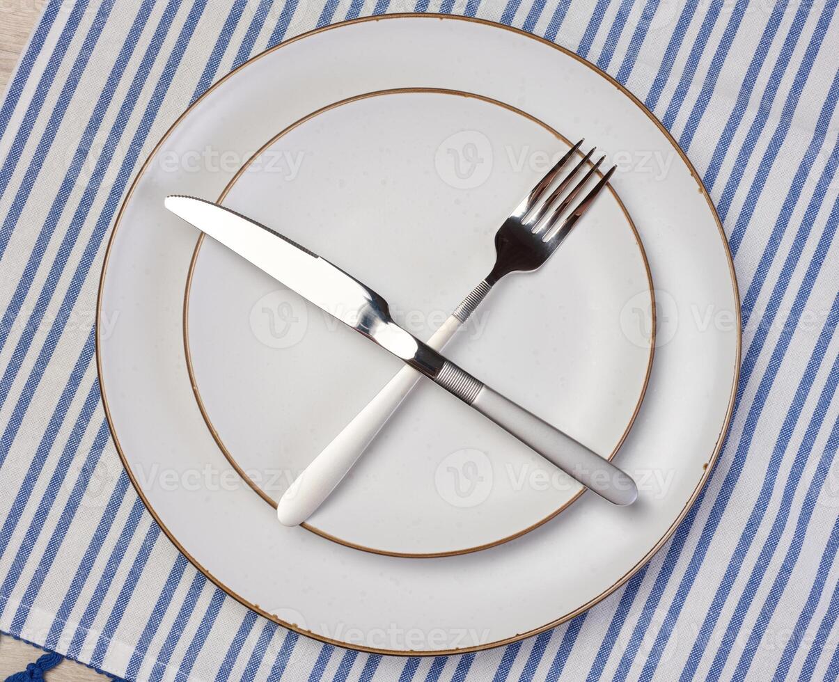 Round empty white ceramic plate, knife and fork crossed, top view photo