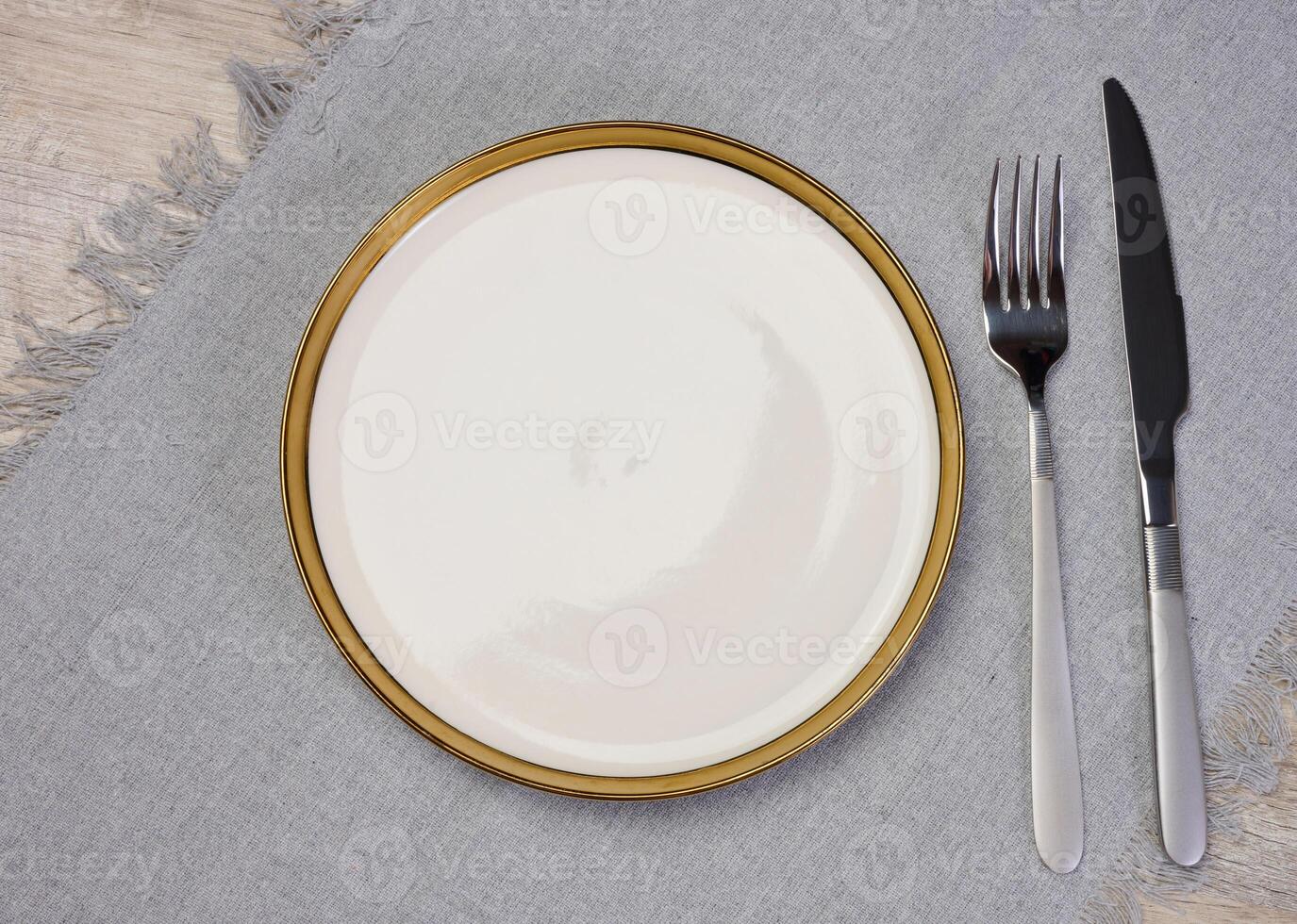 Round empty white ceramic plate, knife and fork on the table, top view photo