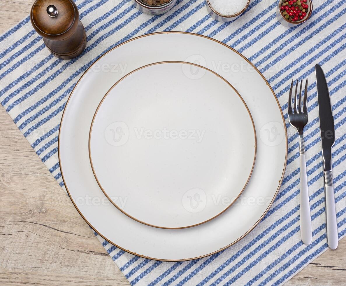Round empty white ceramic plate, knife and fork on the table, top view photo