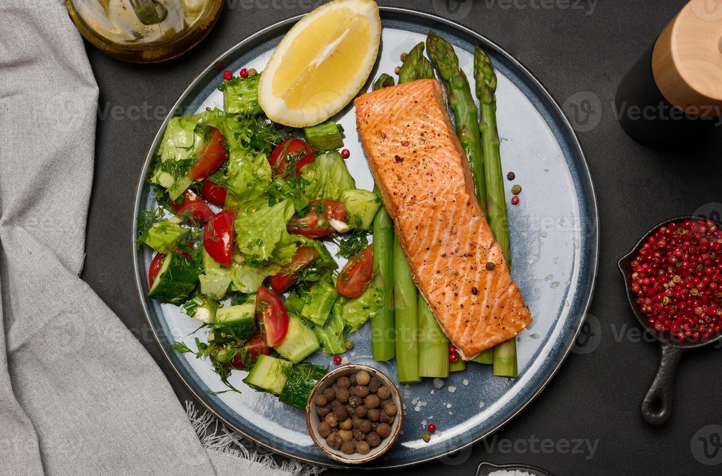 Healthy lunch with grilled salmon with asparagus and fresh tomato and cucumber salad, a row of lemon slice. photo