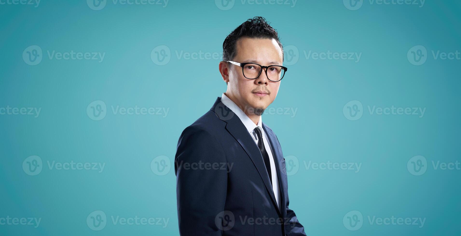 Portrait of a serious businessman with glasses, standing against blue background photo