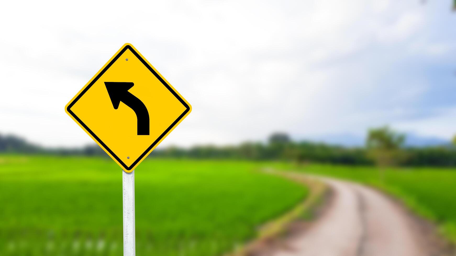 A black left-curved arrow is displayed on a bright yellow sign. photo